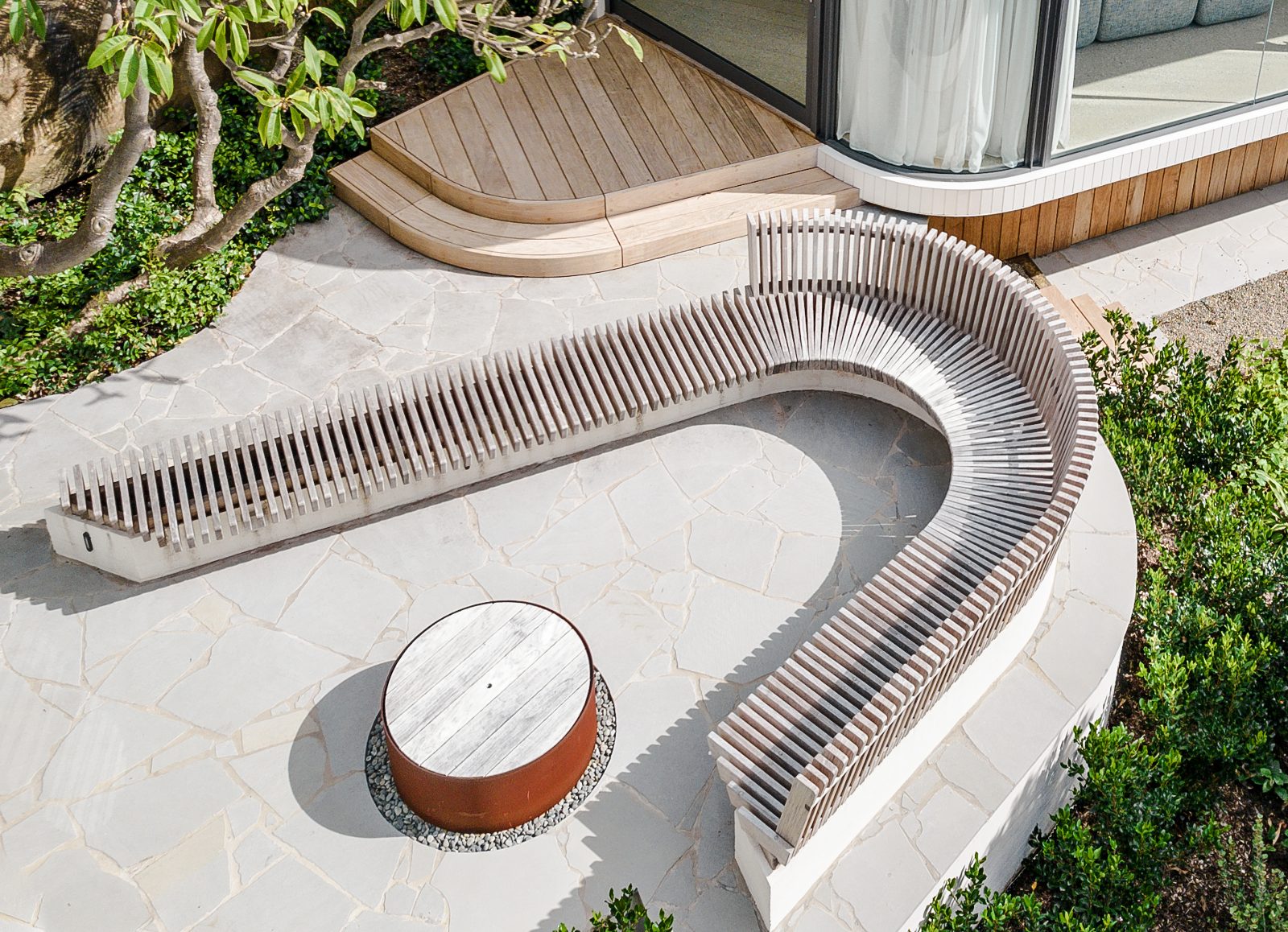 Curved slatted outdoor seat on a concrete plinth around a fire pit, seen from above